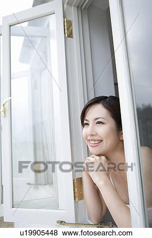Stock Photo - Young woman with hands under chin, looking out window, side view . Fotosearch