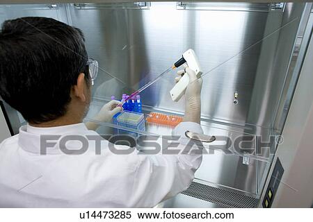 Stock Photography - Male scientist dropping liquids into a micro test tube, rear view, high angle view. Fotosearch
