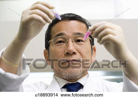Picture - Male scientist holding and looking at micro test tubes with liquid, front view. Fotosearch