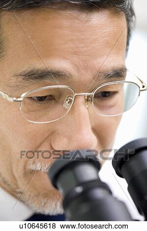 Stock Photo - Male scientist looking through a microscope, front view, close up. Fotosearch