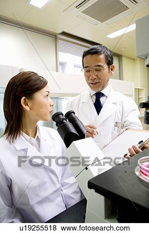 Male scientist talking to female scientist sitting in front of a microscope, front view, side view View Large Photo Image Stock Photo - Male scientist talking to female scientist sitting in front of a microscope, front view, side view. Fotosearch