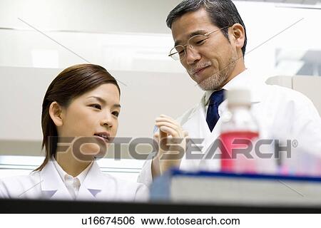 Stock Photograph - Two scientists smiling and looking at micro test tube in laboratory, low angle view, front view. Fotosearch