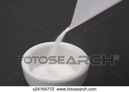 Stock Image - White powders pouring into a mortar, high angle view, black background. Fotosearch