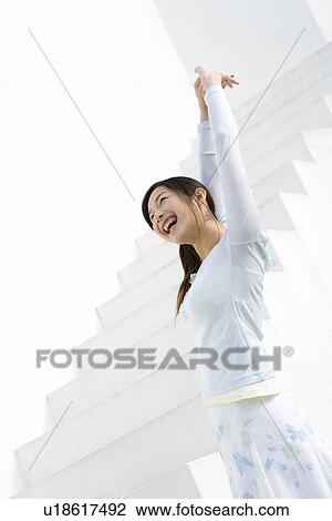 Stock Image - A woman smiling and stretching arms at the stairs, side view, low angle view. Fotosearch