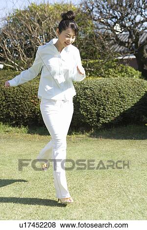 Stock Photo - Woman running in garden, smiling, front view. Fotosearch