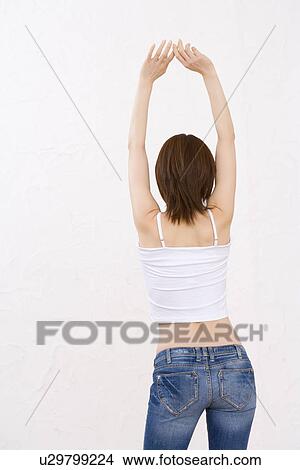 Picture - Woman wearing jeans, stretching arms above head, rear view. Fotosearch