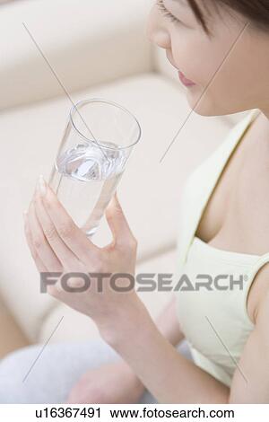 Stock Image - Young woman holding a cup of water, high angle view. Fotosearch