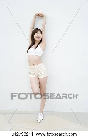Stock Image - Young woman stretching arms above head, front view. Fotosearch