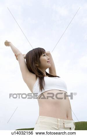 Young woman under the sky, stretching arms above head, low angle view View Large Photo Image Stock Photograph - Young woman under the sky, stretching arms above head, low angle view. Fotosearch