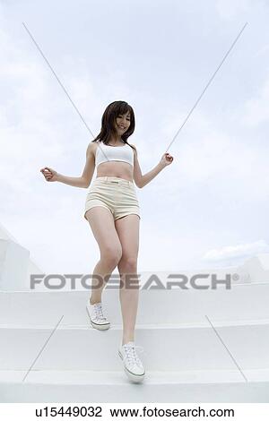 Stock Image - Young woman walking down steps, low angle view . Fotosearch
