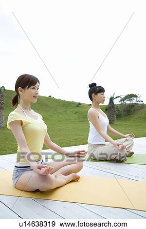 Stock Photo - Young women sitting cross-legged, doing yoga exercise, side view. Fotosearch
