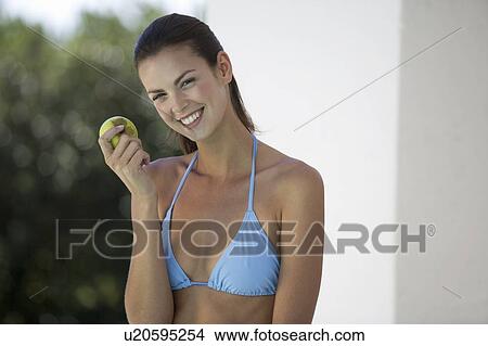 A woman in a bikini eating an apple View Large Photo Image Picture - A woman in a bikini eating an apple. Fotosearch