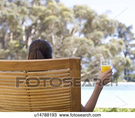 A woman sitting in a sun lounger drinking fruit juice View Large Photo Image Stock Image - A woman sitting in a sun lounger drinking fruit juice. Fotosearch