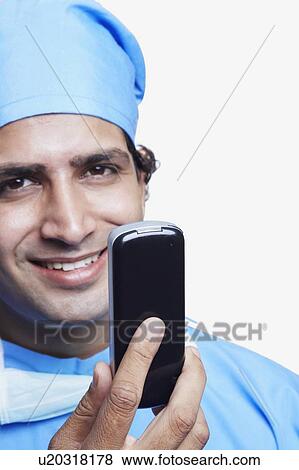 Portrait of a male doctor wearing surgical scrubs and holding a mobile phone View Large Photo Image Stock Photo - Portrait of a male doctor wearing surgical scrubs and holding a mobile phone. Fotosearch
