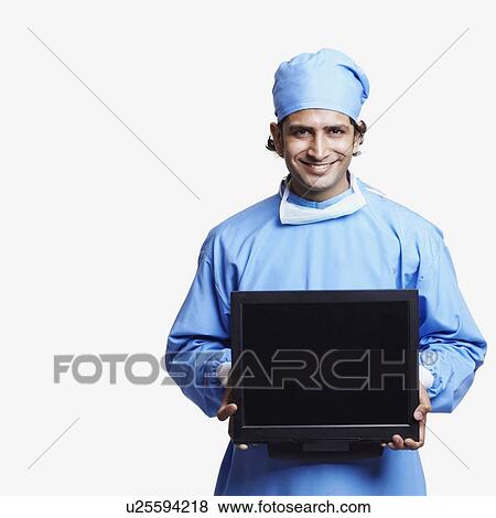 Portrait of a male doctor wearing surgical scrubs and holding a laptop View Large Photo Image Stock Photo - Portrait of a male doctor wearing surgical scrubs and holding a laptop. Fotosearch