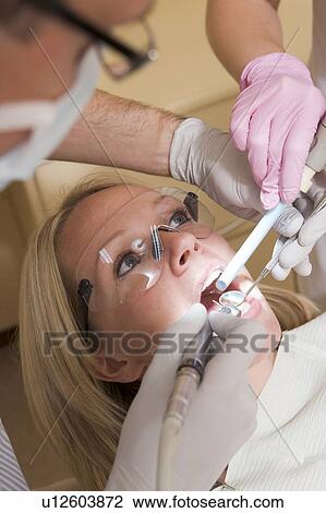Stock Image - Dentist and assistant in exam room with woman in chair. Fotosearch