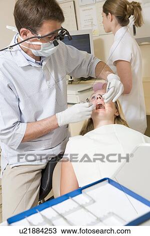 Stock Image - Dentist and assistant in exam room with woman in chair. Fotosearch