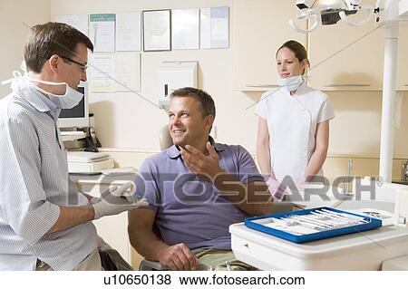 Dentist and assistant in exam room with man in chair smiling View Large Photo Image Stock Photo - Dentist and assistant in exam room with man in chair smiling. Fotosearch