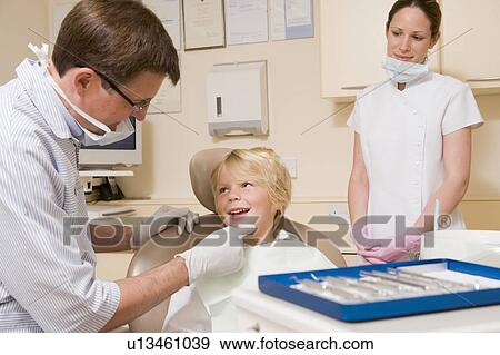 Stock Photo - Dentist and assistant in exam room with young boy in chair. Fotosearch