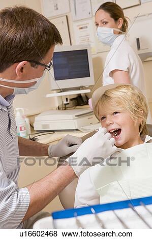 Dentist and assistant in exam room with young boy in chair View Large Photo Image Stock Photo - Dentist and assistant in exam room with young boy in chair. Fotosearch