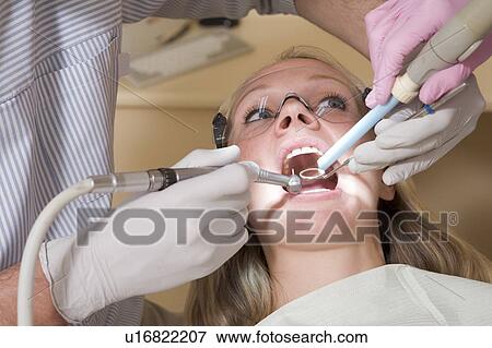 Stock Photo - Dentist and assistant in exam room with woman in chair. Fotosearch