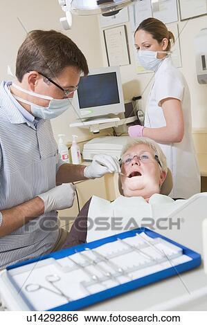 Stock Photograph - Dentist and assistant in exam room with woman in chair. Fotosearch
