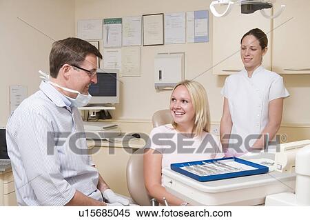Stock Photography - Dentist and assistant in exam room with woman in chair smiling. Fotosearch