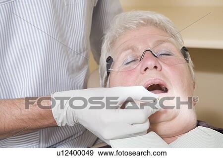 Dentist in exam room fitting dentures on woman in chair View Large Photo Image Stock Photo - Dentist in exam room fitting dentures on woman in chair. Fotosearch