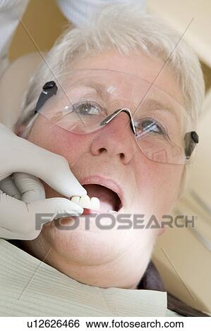 Stock Photograph - Dentist in exam room fitting dentures on woman in chair. Fotosearch