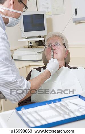 Stock Image - Dentist in exam room with woman in chair. Fotosearch