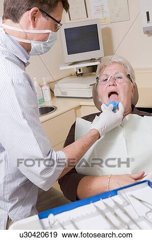 Stock Photo - Dentist in exam room with woman in chair. Fotosearch