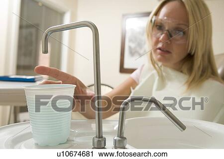 Woman in dental exam room reaching for water View Large Photo Image Stock Image - Woman in dental exam room reaching for water. Fotosearch