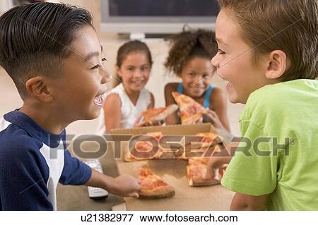 Stock Photo - Four young children indoors eating pizza smiling. Fotosearch