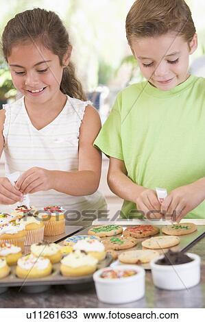 Stock Image - Two children in kitchen decorating cookies smiling. Fotosearch