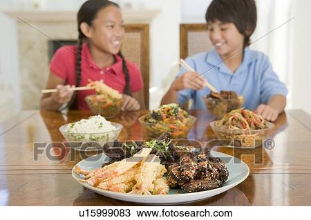 Stock Image - Two young children eating chinese food in dining room smiling. Fotosearch