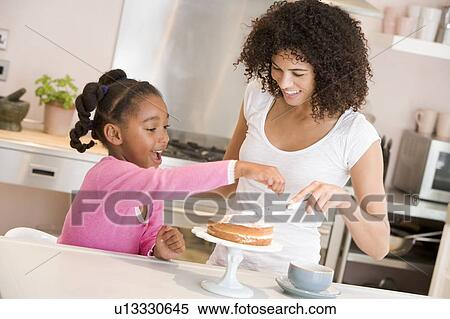 Stock Photography - Woman and young girl in kitchen icing a cake smiling. Fotosearch