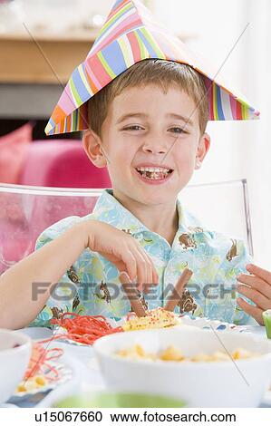 Young boy at party sitting at table with food smiling View Large Photo Image Stock Image - Young boy at party sitting at table with food smiling. Fotosearch