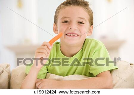Young boy eating carrot stick in living room smiling View Large Photo Image Picture - Young boy eating carrot stick in living room smiling. Fotosearch