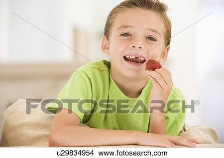 Picture - Young boy eating strawberries in living room smiling. Fotosearch