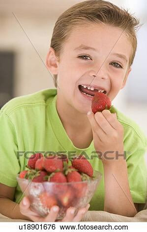 Stock Photograph - Young boy eating strawberries in living room smiling. Fotosearch