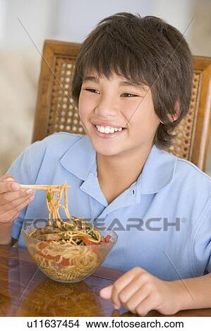 Young boy in dining room eating chinese food smiling View Large Photo Image Picture - Young boy in dining room eating chinese food smiling. Fotosearch