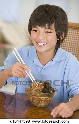 Stock Photo - Young boy in dining room eating chinese food smiling. Fotosearch