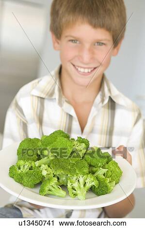 Young boy in kitchen eating broccoli smiling View Large Photo Image Stock Image - Young boy in kitchen eating broccoli smiling. Fotosearch