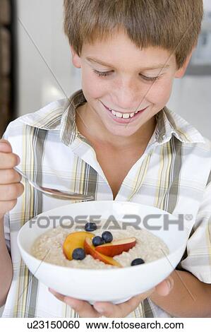Stock Image - Young boy in kitchen eating oatmeal with fruit smiling. Fotosearch