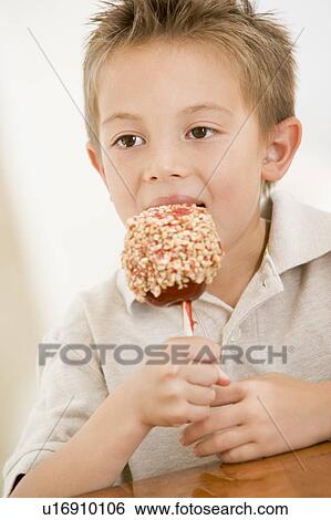 Stock Photograph - Young boy indoors eating candy apple. Fotosearch