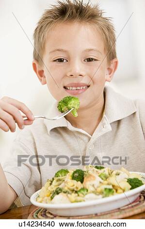 Young boy indoors eating pasta with brocolli smiling View Large Photo Image Stock Image - Young boy indoors eating pasta with brocolli smiling. Fotosearch