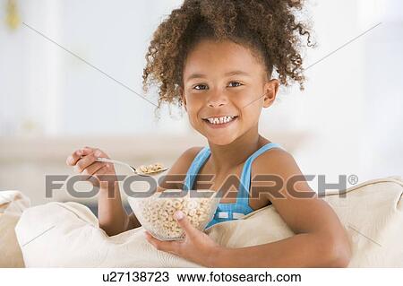 Young girl eating cereal in living room smiling View Large Photo Image Stock Image - Young girl eating cereal in living room smiling. Fotosearch