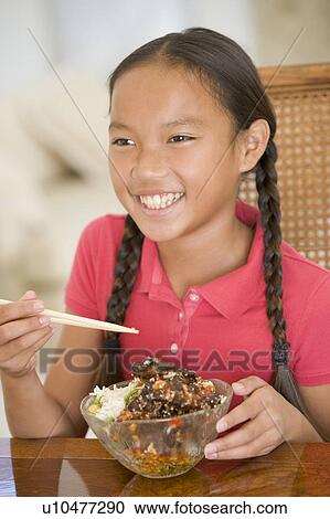 Stock Image - Young girl in dining room eating chinese food smiling. Fotosearch