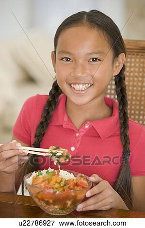 Stock Photo - Young girl in dining room eating chinese food smiling. Fotosearch