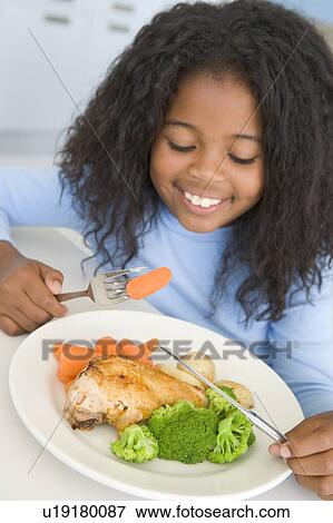 Stock Photo - Young girl in kitchen eating chicken and vegetables smiling. Fotosearch